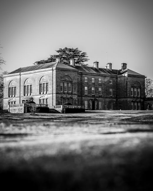 A large brick residential building viewed from the backyard on a cloudy day, with four prominent brick chimneys rising from the roof. The building features multiple white-framed windows, including two tall arched windows on the lower level and smaller rectangular windows on the upper floor. The roof is pitched and covered with weathered tiles, with some areas showing moss or dirt accumulation. The sky above is dark and overcast, suggesting impending storm or evening light. The scene captures the exterior of a historic or traditional house, likely part of a property involving home relocation or furniture transport processes, as seen by the surrounding brick walls and open yard. This setting is indicative of the type of property serviced by Man with Van Hadley Wood during house removals and large property moves, emphasizing the scope of logistics involved in home relocation projects.